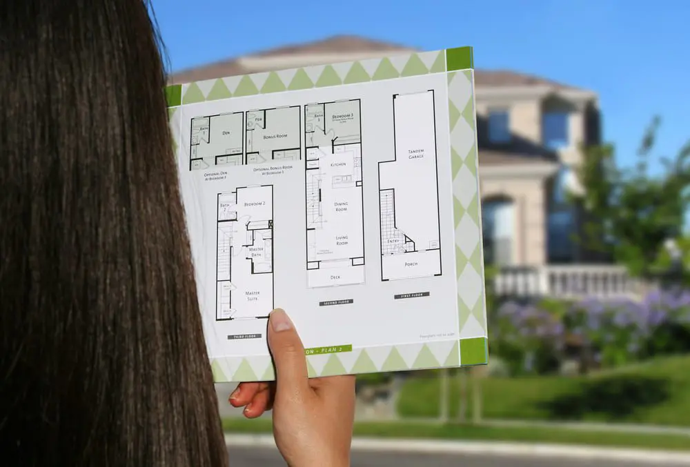 A woman considers the floor plan to her home, wondering how much does an outdoor kitchen costs to build in her backyard.