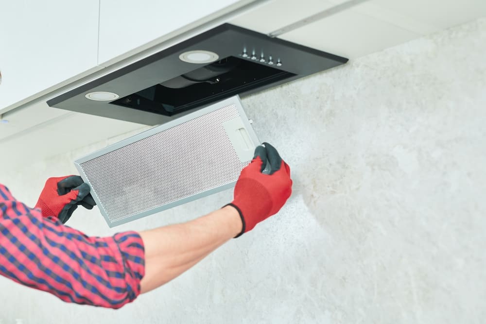 A man wearing protective gloves slowly lowers the panel from his range hood so that he can clean the range hood’s filters.