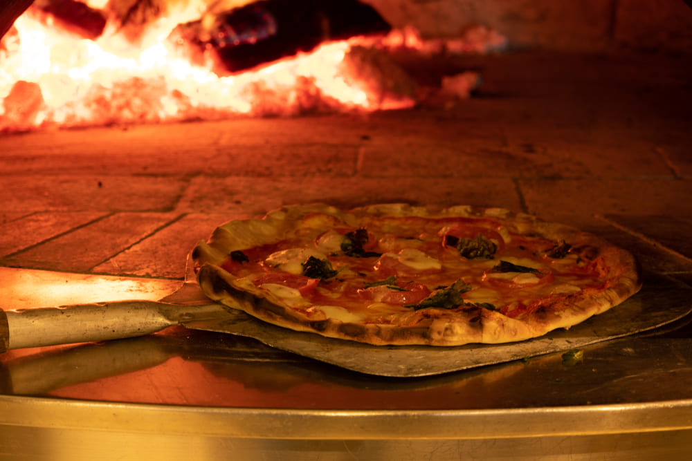 A person off camera, learning how to use a pizza oven by placing their first on a pizza peel onto the bricks A person off camera, learning how to use a pizza oven by placing their first on a pizza peel onto the bricks