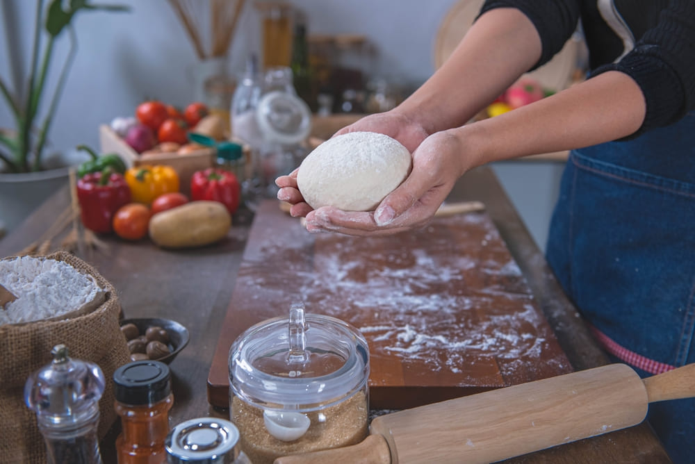 A woman learning to use a pizza oven, using her hands to knead pizza dough