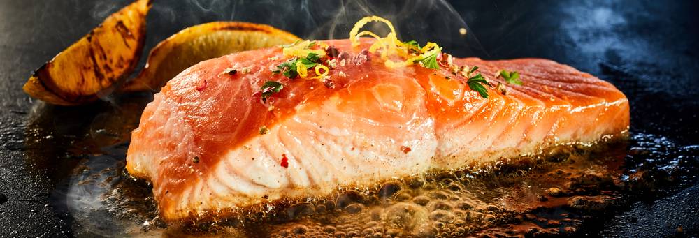 A gorgeously moist, tender, and flaky piece of salmon, skin-side down, being cooked on the even heat of a griddle, a key difference between the griddle vs. grill choice.