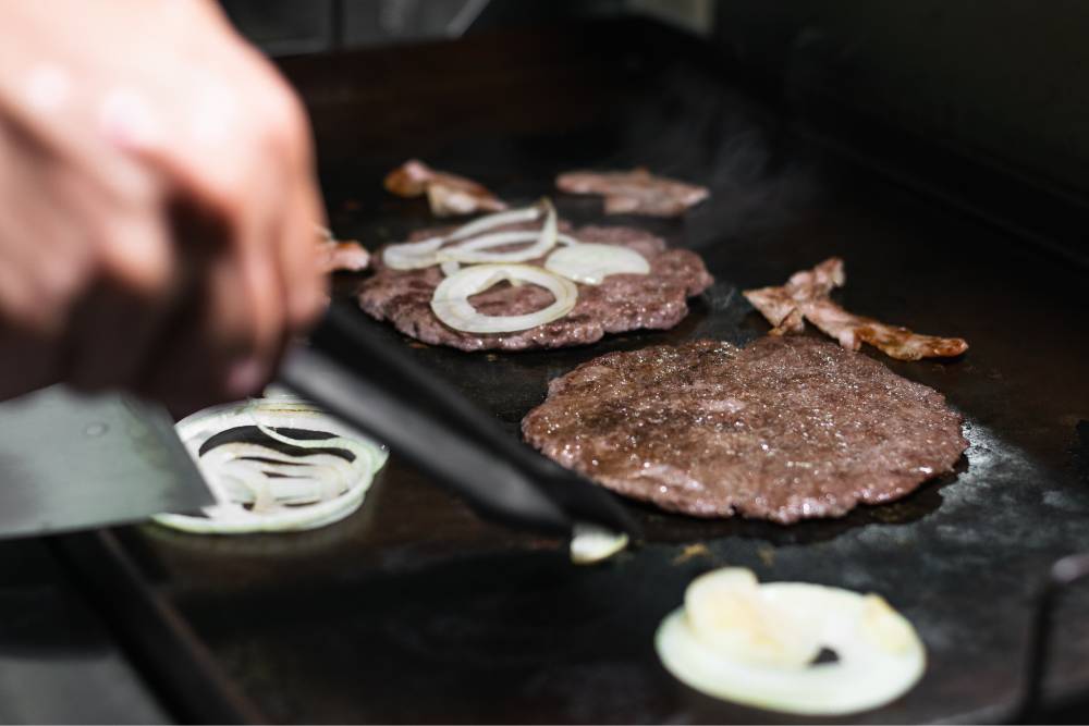 Close-up shot of two smash burgers being cooked on the griddle, an important distinction in the griddle vs. grill debate for certain foods.